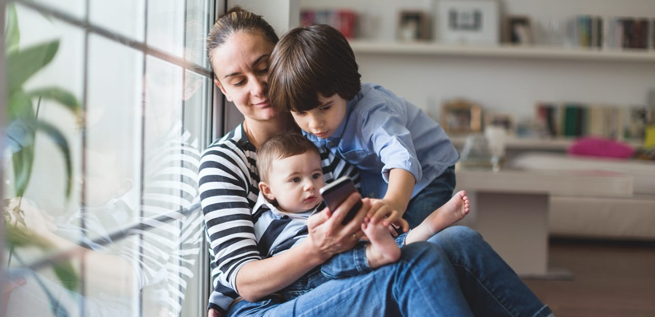 A mother holding two children looking at her phone.