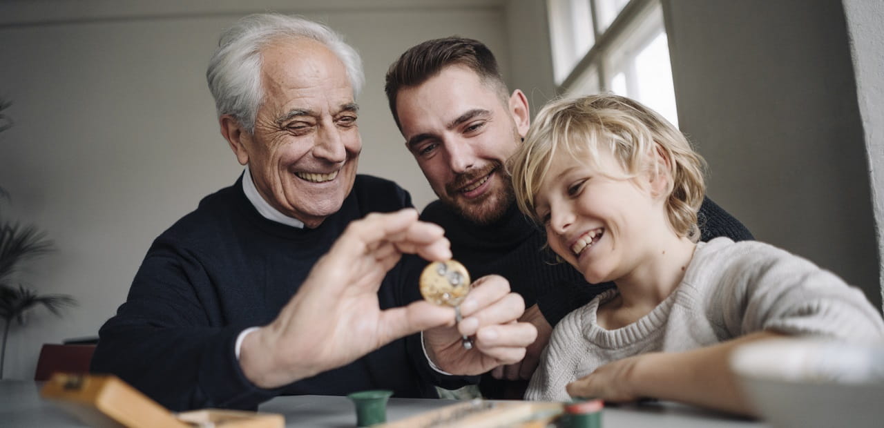 Happy watchmaker showing clockwork to young man and boy