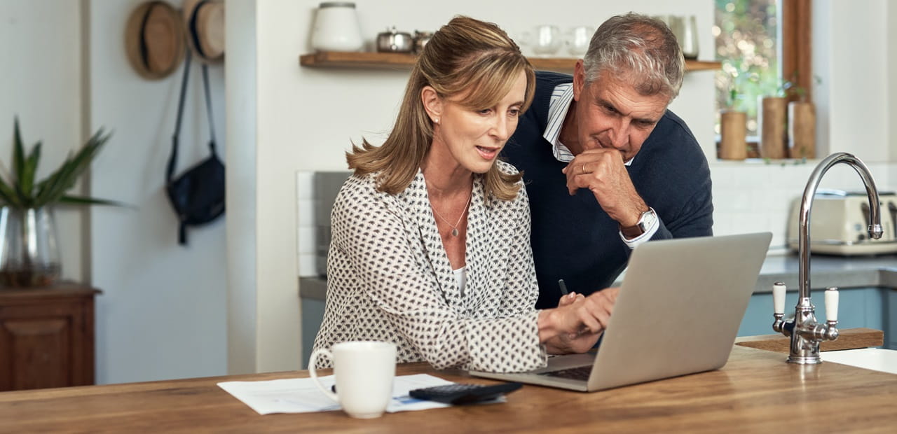 A mature couple planning their finance and paying bills while using a laptop at home.