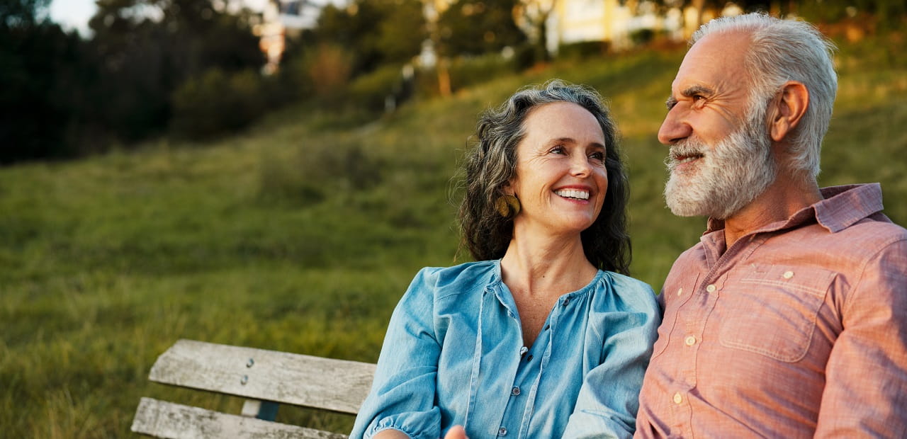 A mature, smiling couple seated beside one another outside