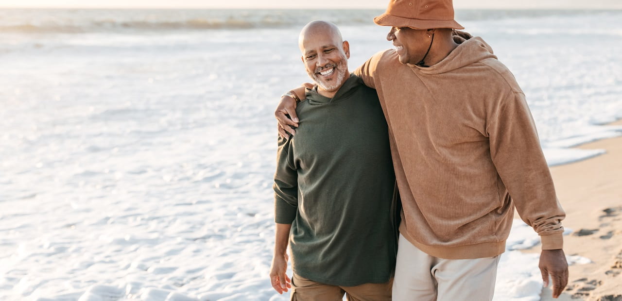 Male couple walks along the beach while holding each other.